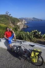 Cyclist pausing on the Belvedere Quattrocchi with a view over the rocks Faraglione on the island Vulcano