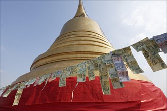 Thai banknotes are hanging on a leash in front of the golden Chedi