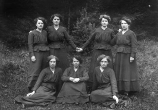 Seven Women Posing in Dark Dresses in the Forest