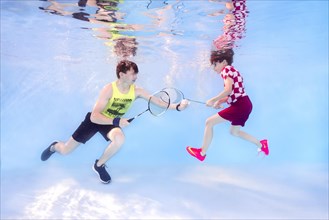 Two teenagers playing badminton underwater