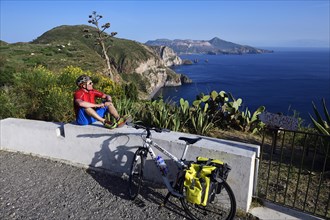 Cyclist pausing on the Belvedere Quattrocchi with a view over the rocks Faraglione on the island Vulcano