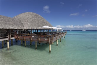 Restaurant on stilts with reed roof in turquoise sea