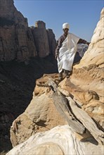 Coptic priest on a rock ledge at the entrance to Abuna Yemata monolithic church
