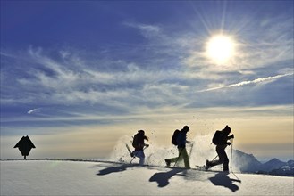 Three snowshoe walkers run in the snow against the light