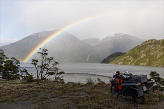 Heavily packed motorcycle in front of a lake behind a rainbow