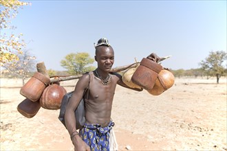 Young Himbamann carries water tank and food on the cattle drive