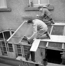 Three roofers repair a canopy with glass panels