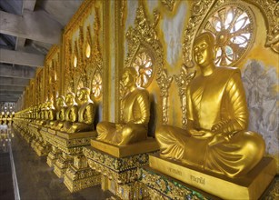 Row of golden Buddha statues in the corridor of the Phra Maha Chedi Chai Mongkhon Pagoda