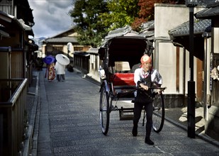 Japanese rickshaw on an old street in Kyoto with a couple wearing kimonos behind