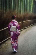 Japanese woman in a purple kimono walking along Arashiyama bamboo forest