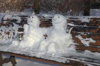 Snowman and snowwoman on a bench with coffee and cigarette butt