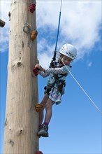 Little girls climbing in climbing equipment with leash and helmet at the climbing tower