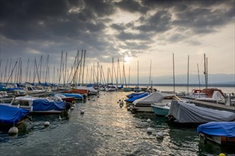 Small boats sheeted and moored along a pontoon on the lake Geneva under a stormy sky
