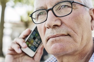 Grey-haired senior with glasses talking on the phone with his smartphone