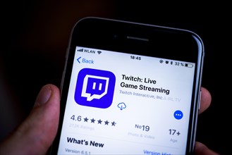 Hand holding iPhone displaying Twitch App in the Apple App Store