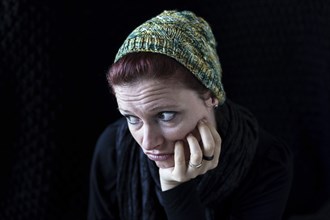 Woman in green wool hat looks disappointed against a black background