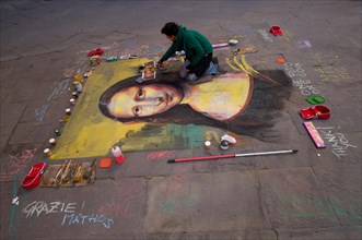 Street artist paints the Mona Lisa by Leonardo da Vinci with chalk on the asphalt