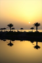 Sunset with water reflection from palm trees and sunshades