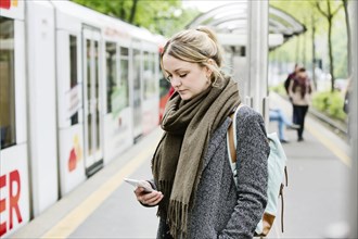 Young woman is waiting with her smartphone in her hand at an S-Bahn station