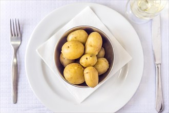 Cooked baby potatoes in silver bowl with cutlery and white wine