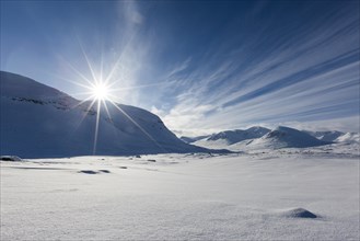 Sun over mountain range in the snow