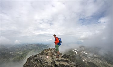 Hiker on the summit of the Hochgolling with rising fog