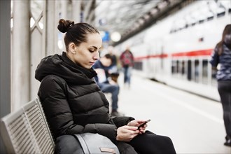 Young woman on a platform in the main station looks at her smartphone