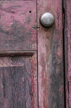 Close-up of old and worn painted red wooden door with silver metal doorknob