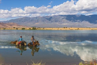 Nomad kids on horses crossing the Tuul river during summer time