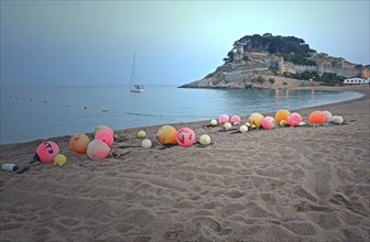 Orange and pink buoys on the sandy beach of Tossa de Mar