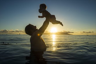 Father playing with his little baby in the water at sunset