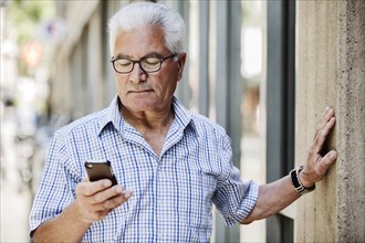 Grey-haired Senior with glasses and smartphone in the city