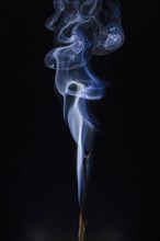 Burned match with blue smoke in front of a dark background