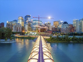 Calgary downtown at dusk with iluminated Peace Bridge and full moon