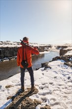 Man with camera equipment looking at Selfoss waterfall in winter