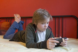 Boy with smartphone is lying on his bed