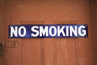 White and blue No Smoking sign on reddish brown wooden entrance door