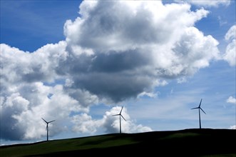 Silhouettes of wind turbines on a hill with cloudy sky