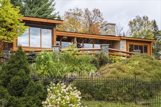 Rear view of luxurious stained cedar and timber wood home with panoramic windows and landscaping in autumn