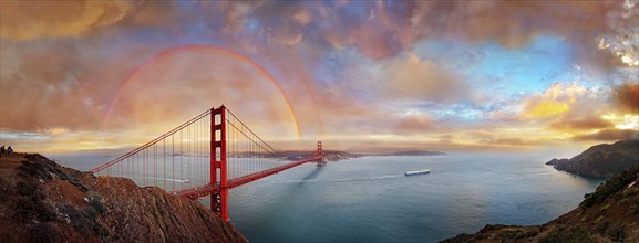 Panorama of the Golden Gate Bridge with rainbow at sunset and orange shining thunderclouds