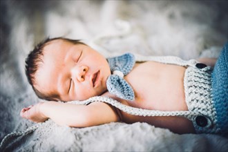 A newborn baby boy sleeping in blue and grey knitted bow tie and trousers