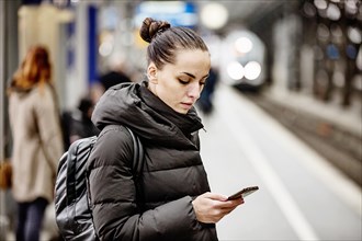 Young woman on a platform in the main station looks at her smartphone