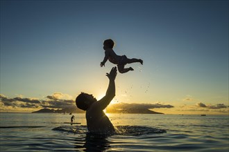 Father playing with his little baby in the water at sunset