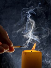 Lighting of a candle with smoking match in front of a black background