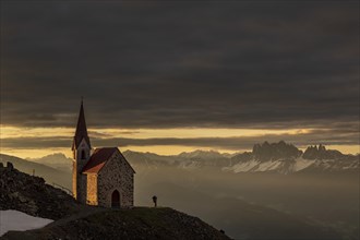 Latzfonser cross chapel at sunrise with dramatic clouds and South Tyrolean mountains