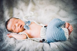 A newborn baby boy sleeping in blue and grey knitted bow tie and trousers