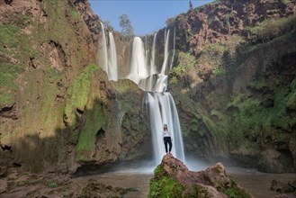 Young woman standing on a stone in front of Ouzoud waterfalls and cascades