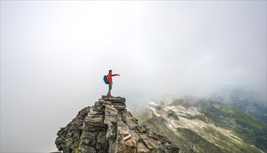 Hiker on the summit of the Hochgolling with rising fog