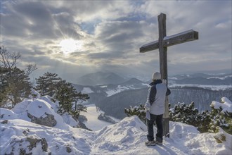 Hiker at summit cross in winter