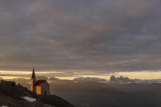 Latzfonser cross chapel at sunrise with clouds and South Tyrolean mountains